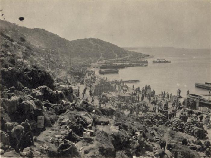 View of the beach at Gaba Tepe where the allied troops landed in the Gallipoli Campaign, World War One. The view shows dugouts, men, landing craft, and piles of stores. Photographed by an unknown photographer in 1915.